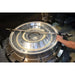 A large circular metallic industrial component or machine part on a workbench, with a person's arm and hand visible at the right side holding a measuring tool.